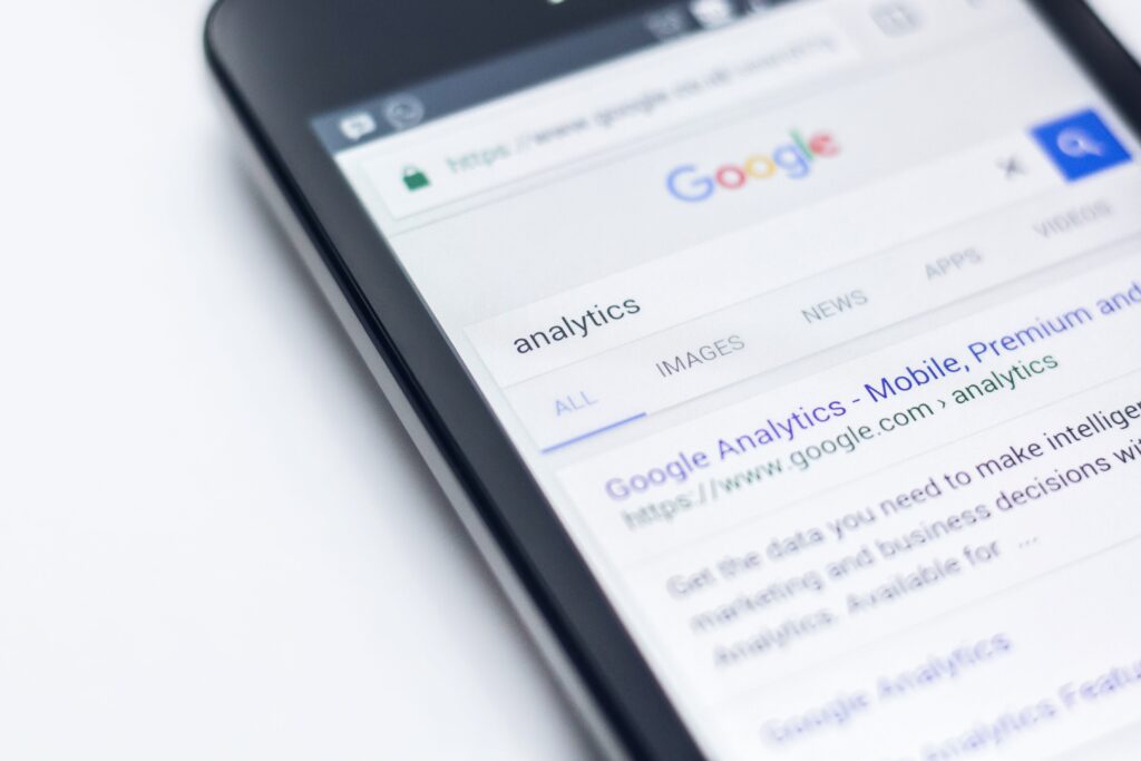 Smartphone displaying Google search results for 'analytics' with the first result for Google Analytics and multiple search tabs like IMAGES and NEWS visible.