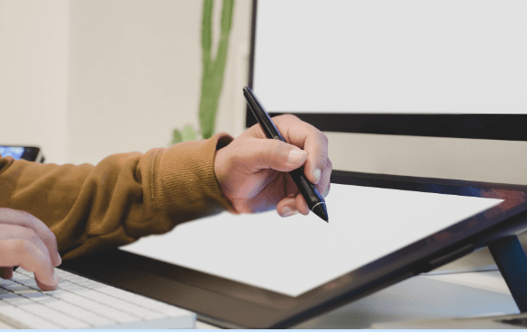 Person using a stylus on a digital drawing tablet with a blank screen next to a keyboard.