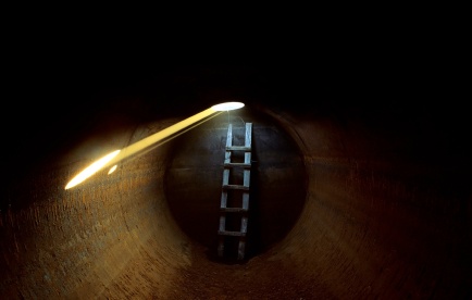 A ladder leading up to a light source in a circular tunnel.