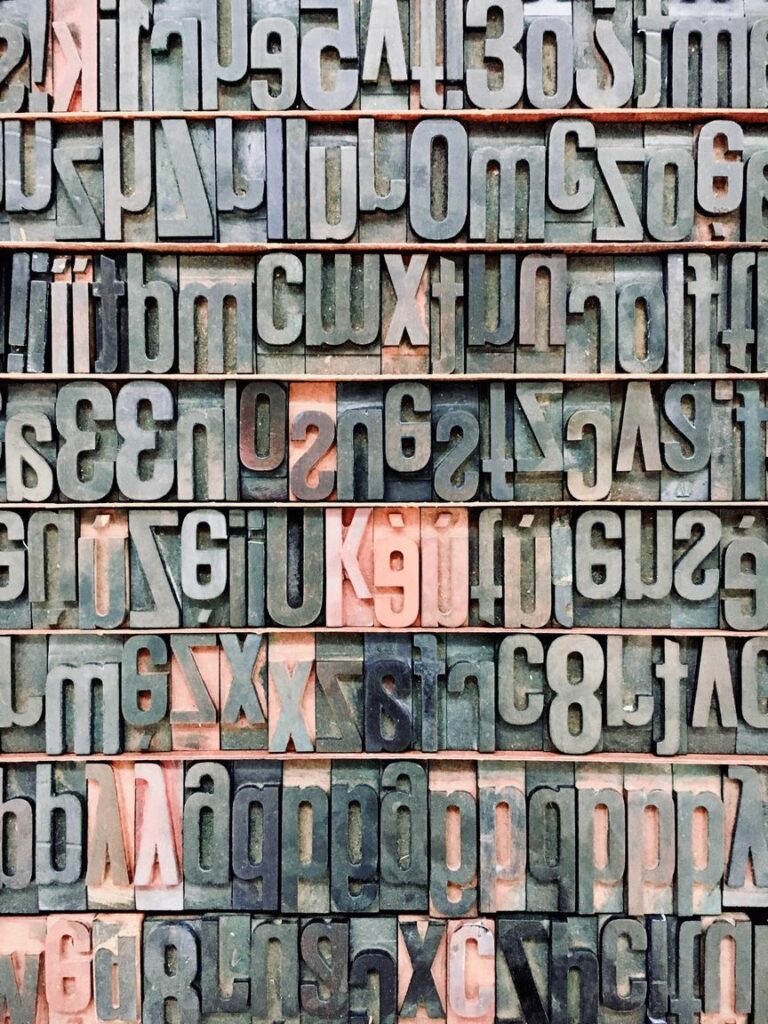 A variety of vintage letterpress printing blocks with reversed letters and numbers in different fonts and sizes, showing ink stains from previous use.