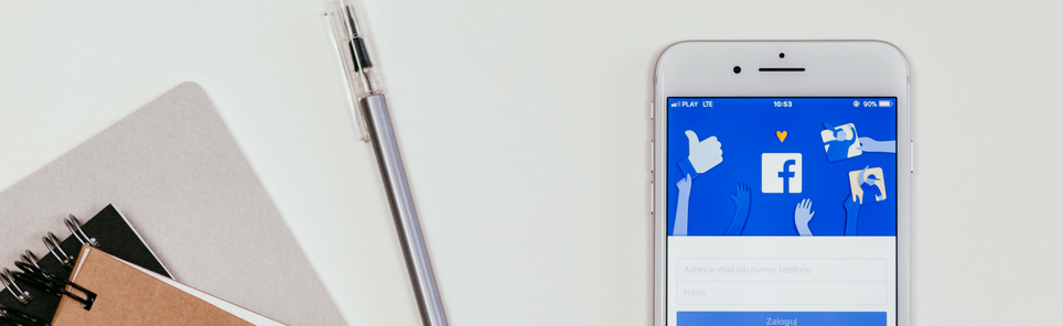 Smartphone displaying Facebook login page beside a notebook and pen on a white surface.