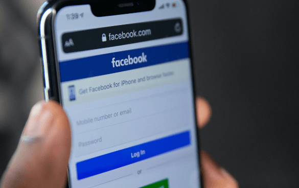 Close-up of a smartphone held in a hand displaying the Facebook login page with fields for mobile number or email and password.
