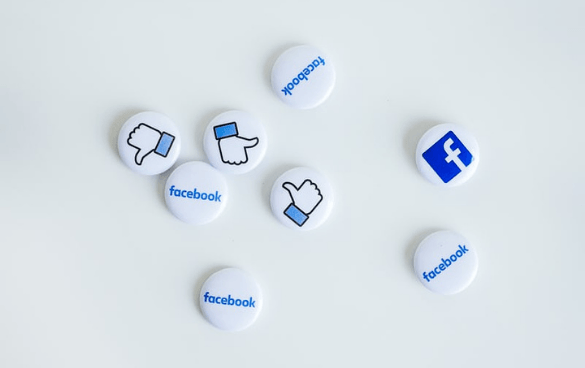 A collection of round pins with Facebook logos and 'Like' icons on a white surface.