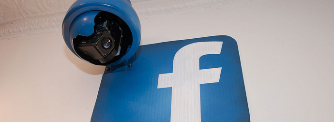 A security camera mounted above a blue Facebook logo sign.