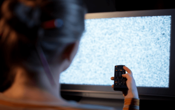 A woman points a remote at a TV with static on the screen