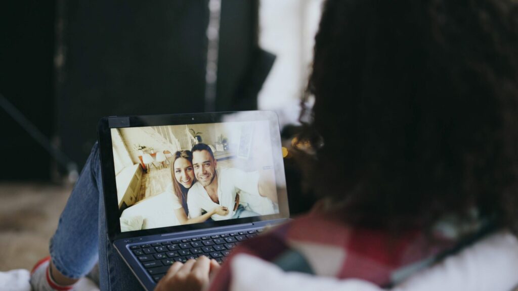 A woman watches as a couple smiles together on a computer screen