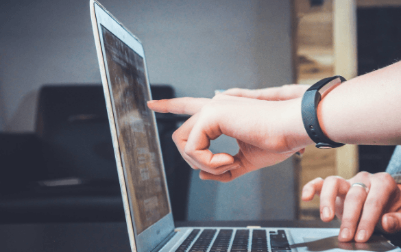 One person pointing at a laptop screen while another person uses the keyboard in an indoor setting.