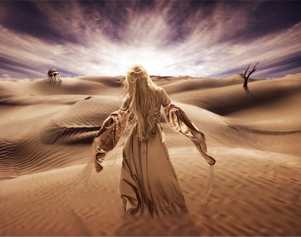 A person with long blonde hair in a flowing robe stands in a desert, facing a dramatic sky with radiating clouds, surrounded by sand dunes and dead trees, all cast in sepia tones.