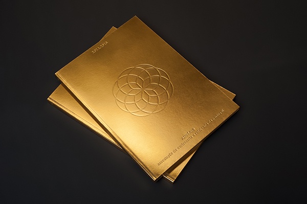 Three stacked golden books with an embossed geometric pattern on the top cover and inscribed text.