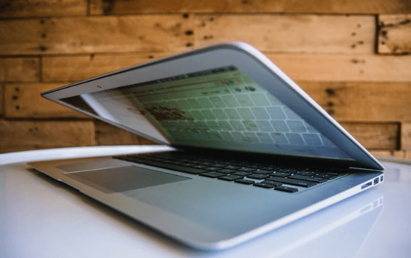 Partially closed laptop on a white surface with the screen visible, against a wooden plank wall background.