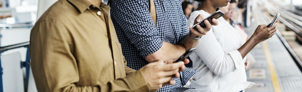 Three people standing in a row, each looking at their own smartphone, possibly waiting at a train station platform.