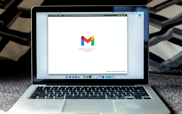 Laptop on a patterned surface displaying the Gmail loading page with the Gmail logo.