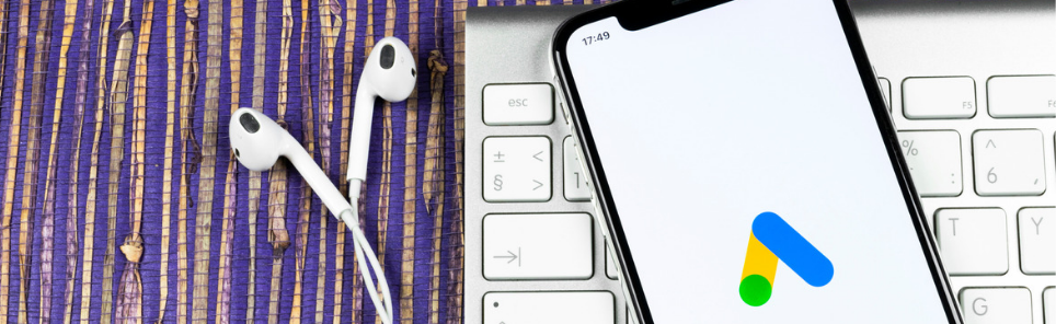 Wired white earbuds on a purple and yellow striped surface to the left, and a smartphone with an app icon on its screen resting on a white keyboard to the right.