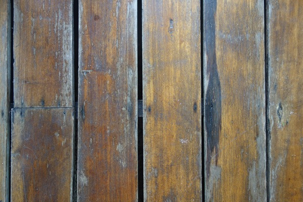 Close-up of a weathered wooden plank surface with varying shades of brown and visible grain patterns.