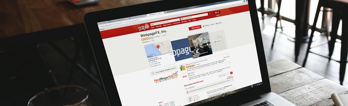 Laptop on a wooden table displaying a company profile page on a Yelp-like website, with a coffee cup to the left of the laptop.