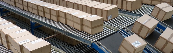 Multiple rows of a conveyor belt system transporting uniformly sized cardboard boxes in a distribution center.