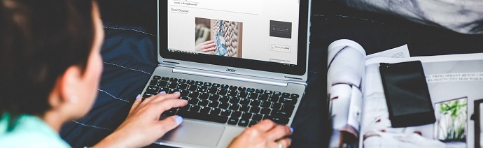 Person using an Acer laptop to browse a photo gallery website with printed materials beside them.