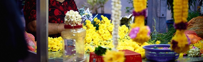 Vibrant yellow marigold flowers arranged for sale with a person in a red patterned garment partially visible in the background.