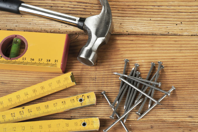 A claw hammer, a yellow folding ruler, a level tool, and scattered nails on a wooden surface.