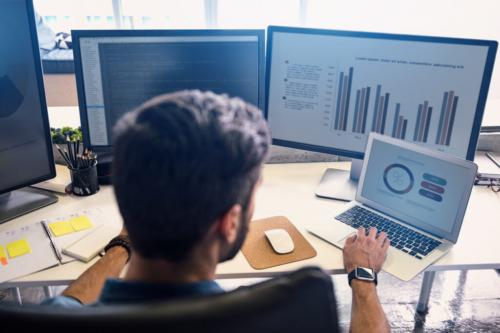 Man creating statistics in modern office. He working on digital devices while sitting at table and turning back to camera