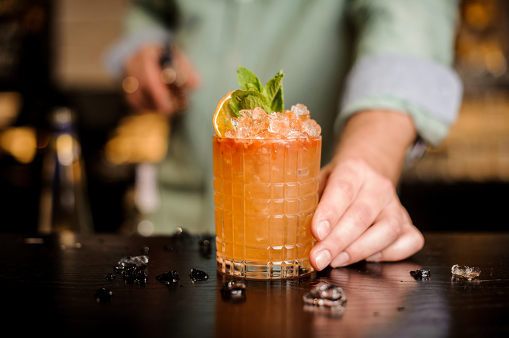 Bartender finished decorating his cocktail with mint and orange slice