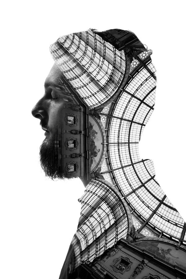 A monochromatic double exposure portrait of a bearded man with the transparent overlay of a grand, ornate building aligning with his profile.