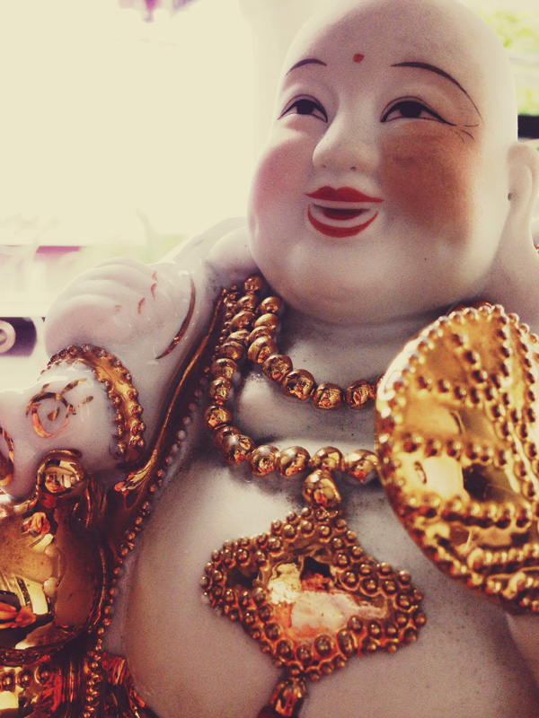 Close-up of a Laughing Buddha figurine with a joyful expression, adorned with golden jewelry, including necklaces and a medallion.