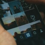 Close-up of hands holding a smartphone displaying a grid of thumbnail images on the screen.