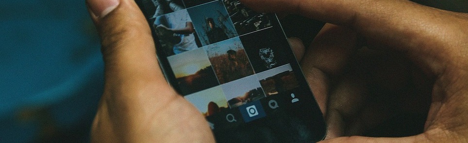 Close-up of hands holding a smartphone displaying a grid of thumbnail images on the screen.