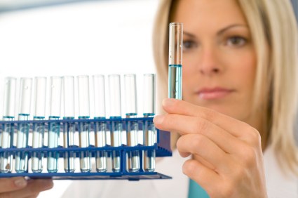 A scientist examining a test tube with a blue liquid, with a rack of additional test tubes in the foreground.