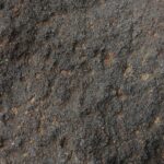 Close-up of a rough, dark gray textured surface resembling rock or asphalt with small lighter specks.