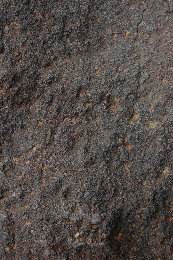 Close-up of a rough, dark gray textured surface resembling rock or asphalt with small lighter specks.