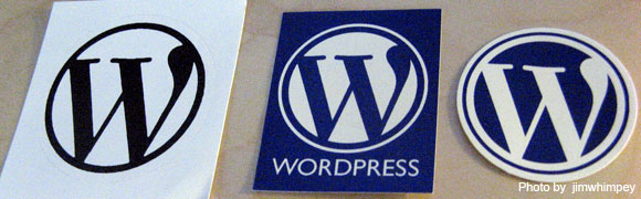 Three variations of the WordPress logo stickers, with the letter 'W' inside a circle, in black and white, blue and white with the brand name, and a three-dimensional blue and white version.