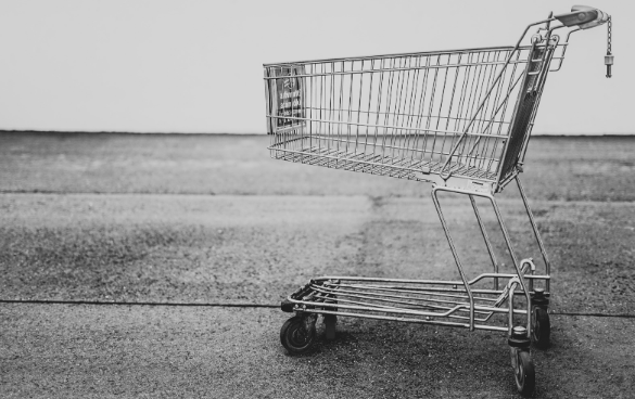 Side view of an empty shopping cart on a flat outdoor surface in a monochromatic setting.