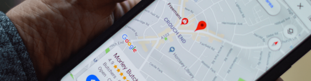 Close-up of a hand holding a smartphone displaying Google Maps focused on the Crouch End area with a red location pin and business ratings visible.