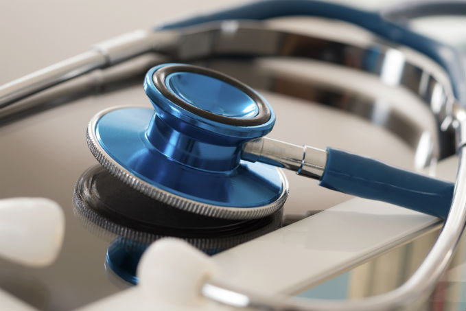 Close-up of a blue stethoscope with its diaphragm in focus on a flat surface, with earpieces visible in the foreground.