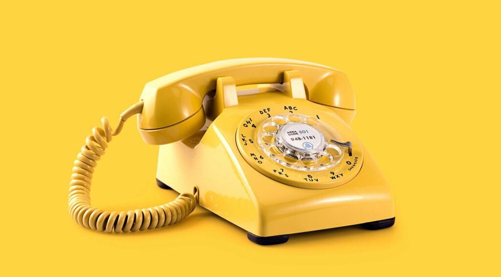 Vintage yellow rotary dial telephone on a matching yellow background.