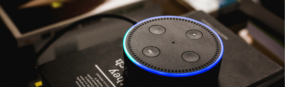 Amazon Echo Dot activated with blue light on top of a black surface.