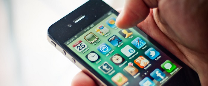 Close-up of a person's hand holding an older model iPhone with a display of colorful app icons.