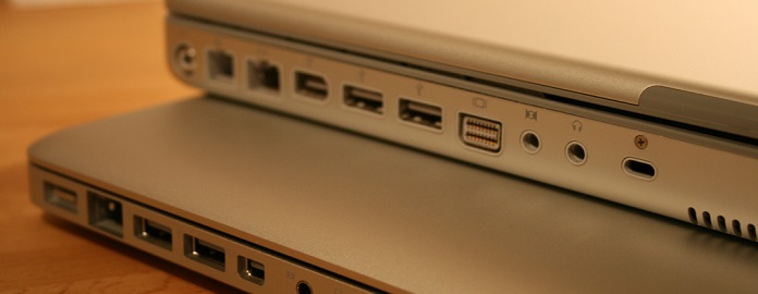 Two laptops stacked with a focus on their side ports, showing an older model with multiple ports on top and a newer model with fewer, USB-C type ports on the bottom.