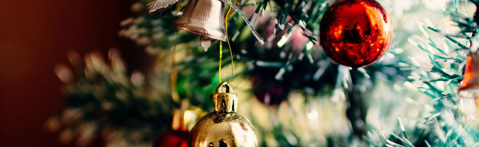 Close-up of a Christmas tree with a focus on a golden bauble, a red bauble in the background, and other festive decorations.