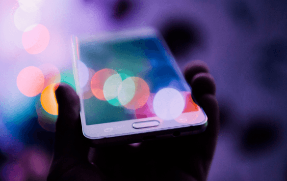 Close-up of hands holding a smartphone with a colorful bokeh light background.