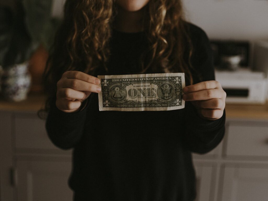 Person holding a one-dollar bill with a kitchen background, face not visible.