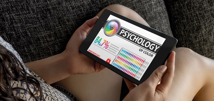 Person holding a tablet displaying a colorful 'PSYCHOLOGY OF COLOR' infographic, with a color wheel and chart on a couch.