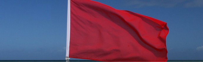 A plain red flag fluttering against a clear blue sky.