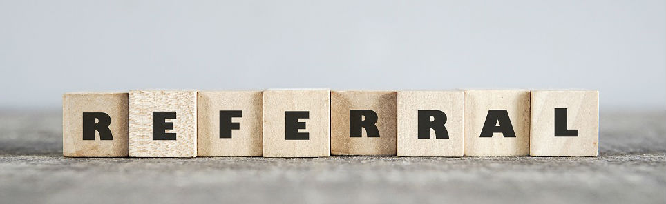 Wooden blocks on a gray surface spelling out the word REFERRAL.