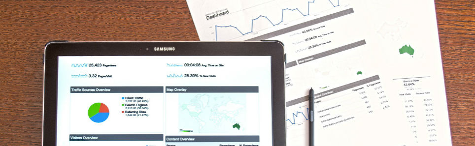 A Samsung tablet showing analytics data with printed data sheets and a pen on a wooden desk.