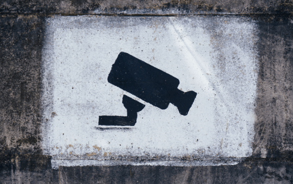 Symbol of a surveillance camera painted in black on a weathered white background.