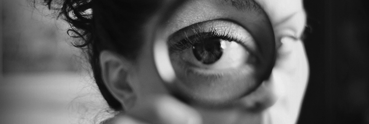 Close-up of a person's eye magnified through a handheld magnifying glass in black and white.