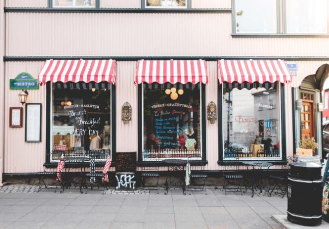 A charming bistro with red and white striped awnings, outdoor seating, and writings on the windows advertising brunch and breakfast.